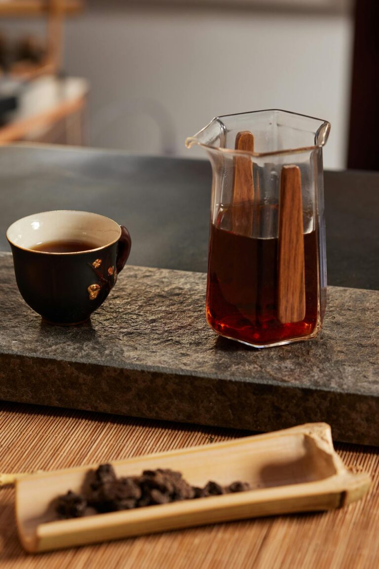 A beautiful tea setup featuring a glass server, a black tea cup, and tea leaves on a bamboo tray.